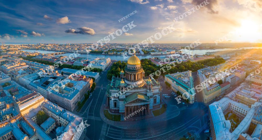Фотография панорамного вида Санкт-Петербург, Россия, снятая с дрона. На изображении запечатлена Исаакиевская площадь с величественным Исаакиевский собор, а также прилегающие улицы исторического центра города. Фотоснимок передаёт масштаб городской застройки, чёткую планировку улиц и архитектурную гармонию Петербурга. Это изображение отражает панораму одного из главных городов Российской Федерации и подчёркивает архитектуру городов России, показанную с высоты.